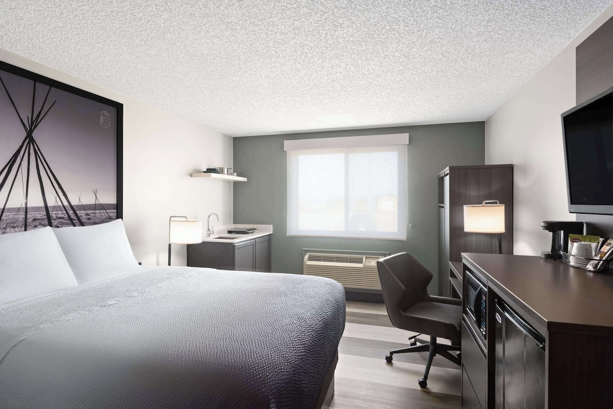 A hotel room with a bed, desk, chair, TV, and a window with a view.