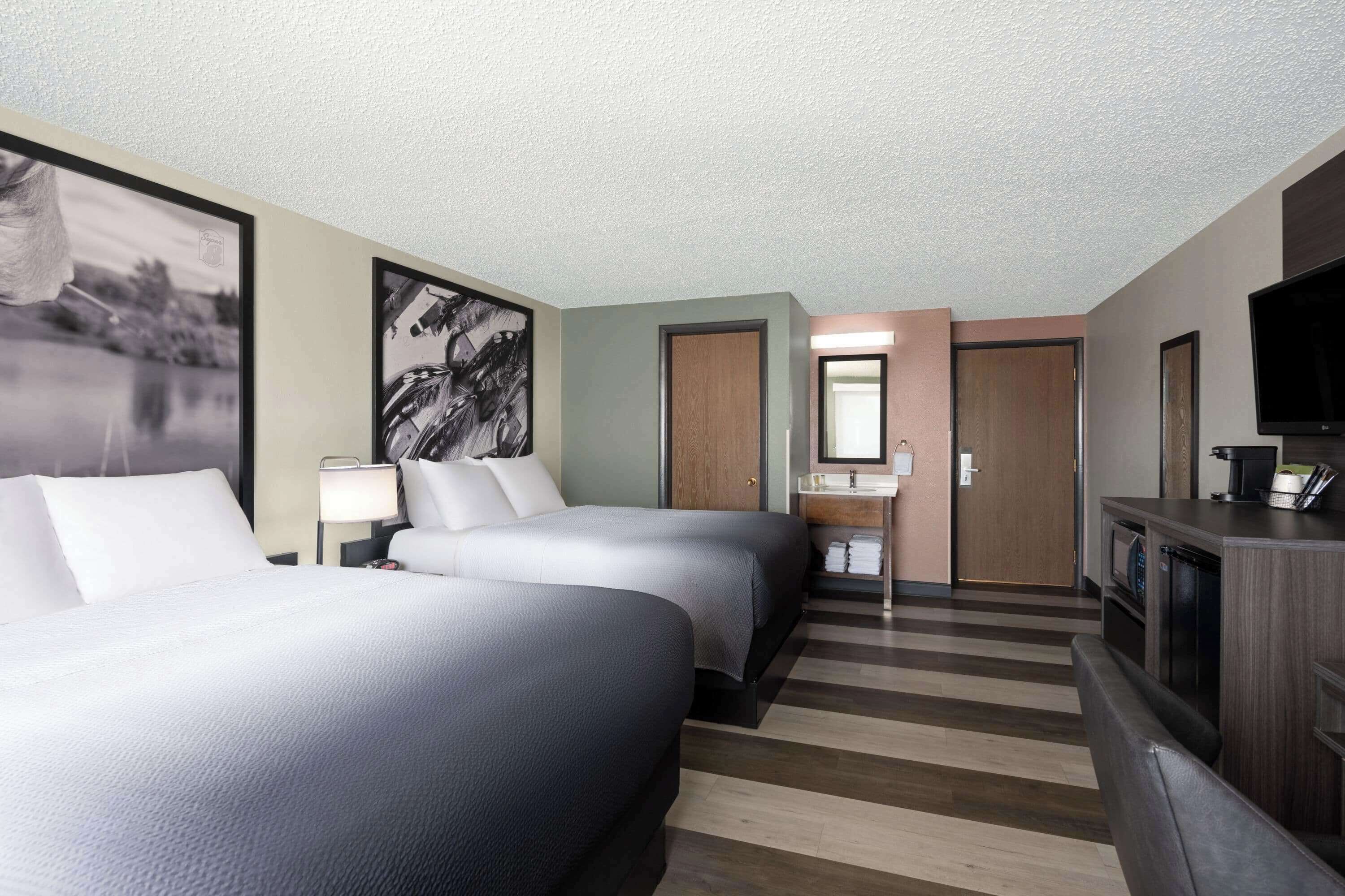 A hotel room with two beds, a TV, a desk, a mirror, and a bathroom door.