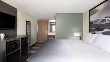 A hotel room with a large bed, a flat-screen TV, a microwave, and a small refrigerator.
