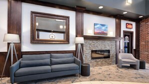 A lobby with a grey sofa, two floor lamps, a fireplace, and a brick wall. - Super 8 by Wyndham Conrad (Conrad)