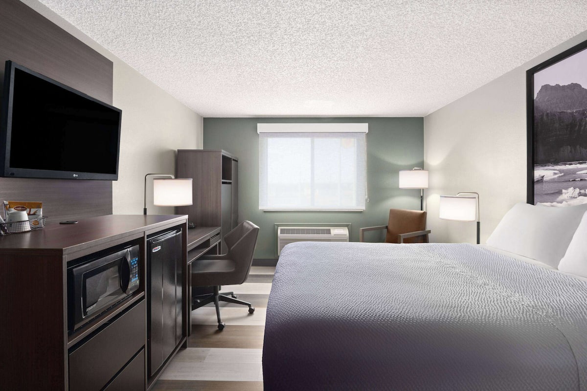 A hotel room with a bed, desk, microwave, refrigerator, TV, and two lamps.