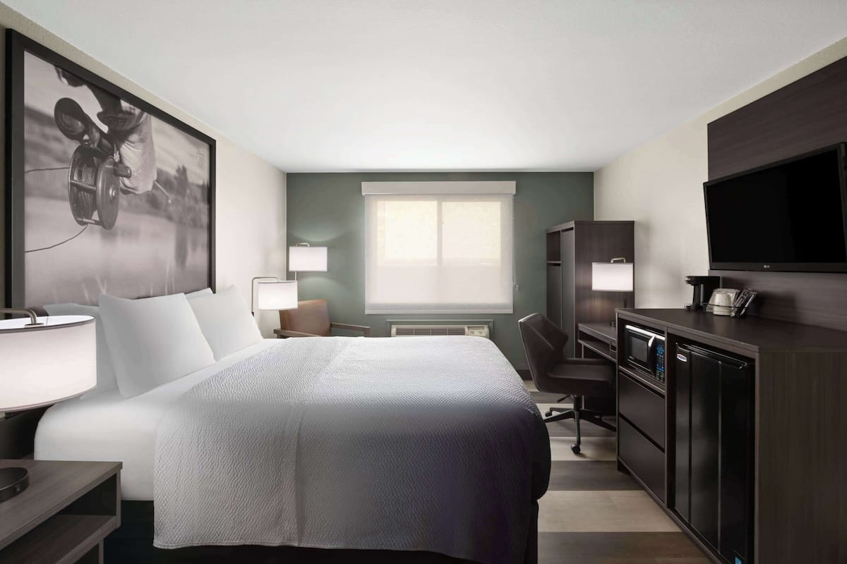 A hotel room with a bed, desk, chair, TV, and kitchenette.