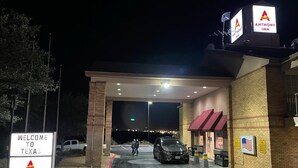 A well-lit hotel entrance with a sign welcoming visitors to Texas, a covered parking area, and a visible American flag. - Anthony Inn (Anthony)