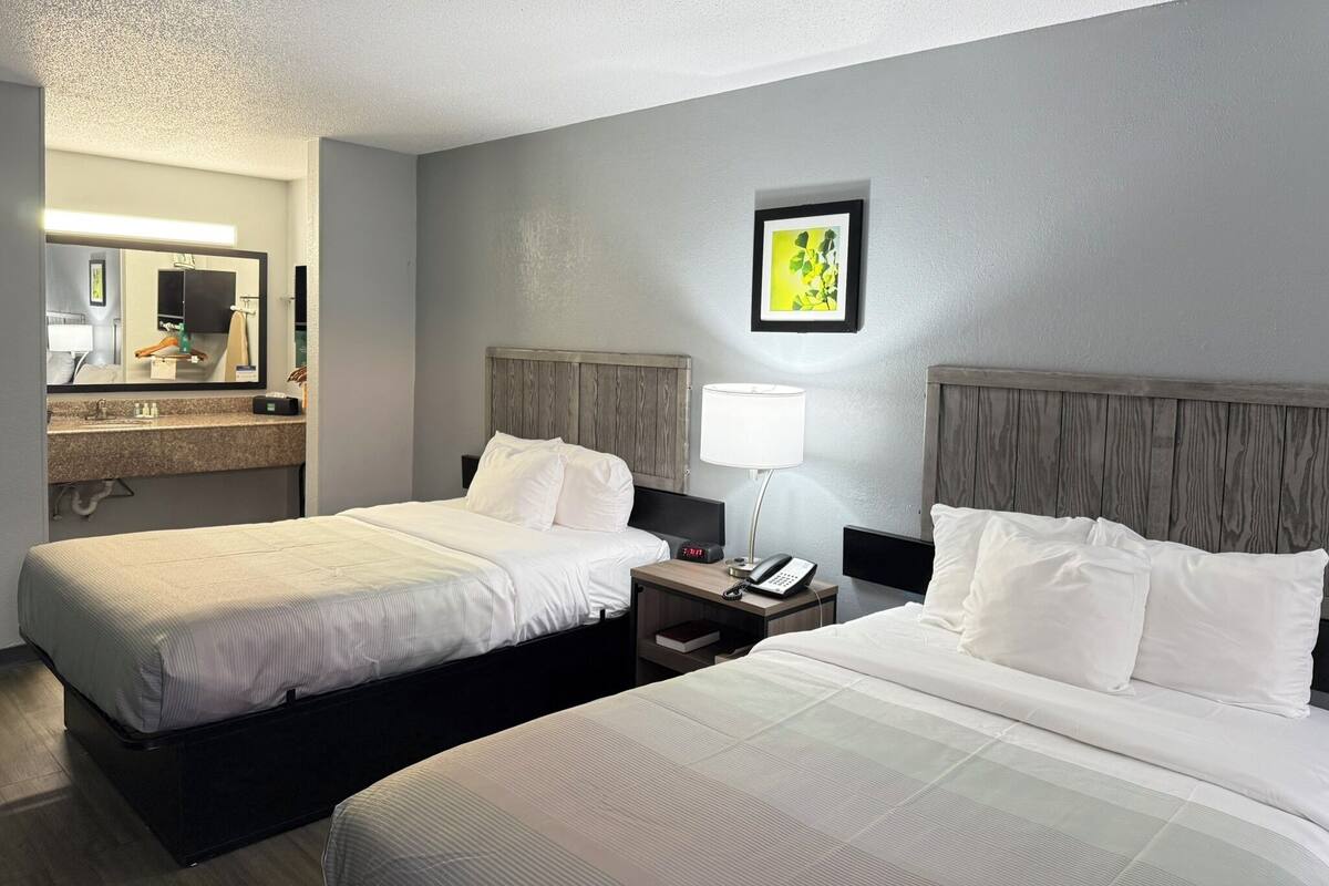 Habitación de hotel con dos camas, una mesita de noche con lámpara, teléfono y espejo.
