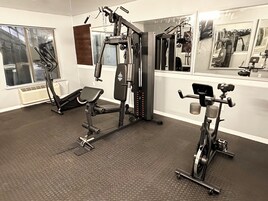 Une salle de sport équipée de divers appareils d’entraînement, notamment un support à squats, un banc de développé couché et un appareil elliptique.
