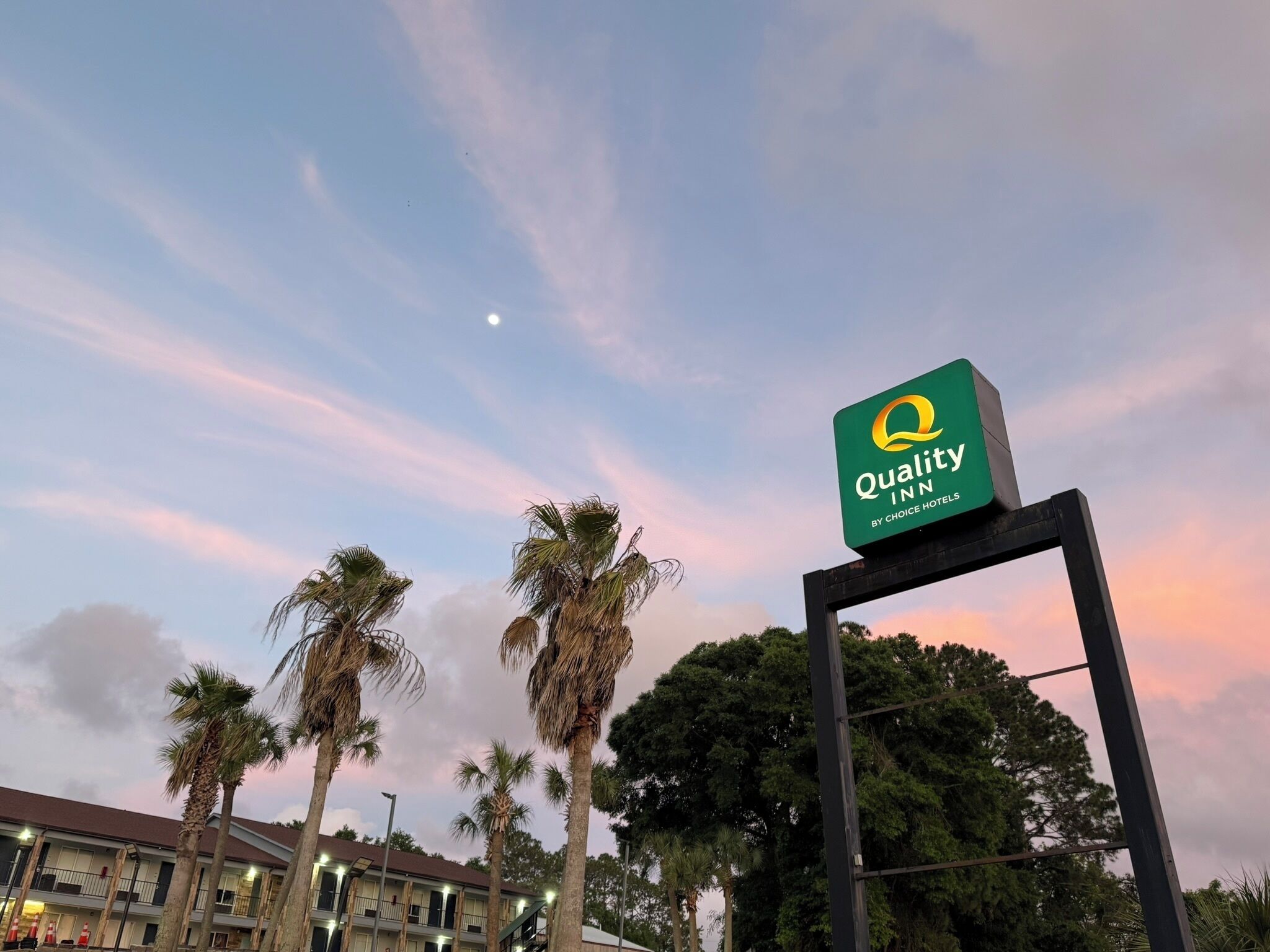 A sign for Quality Inn by Choice Hotels with a clear sky and palm trees in the background.