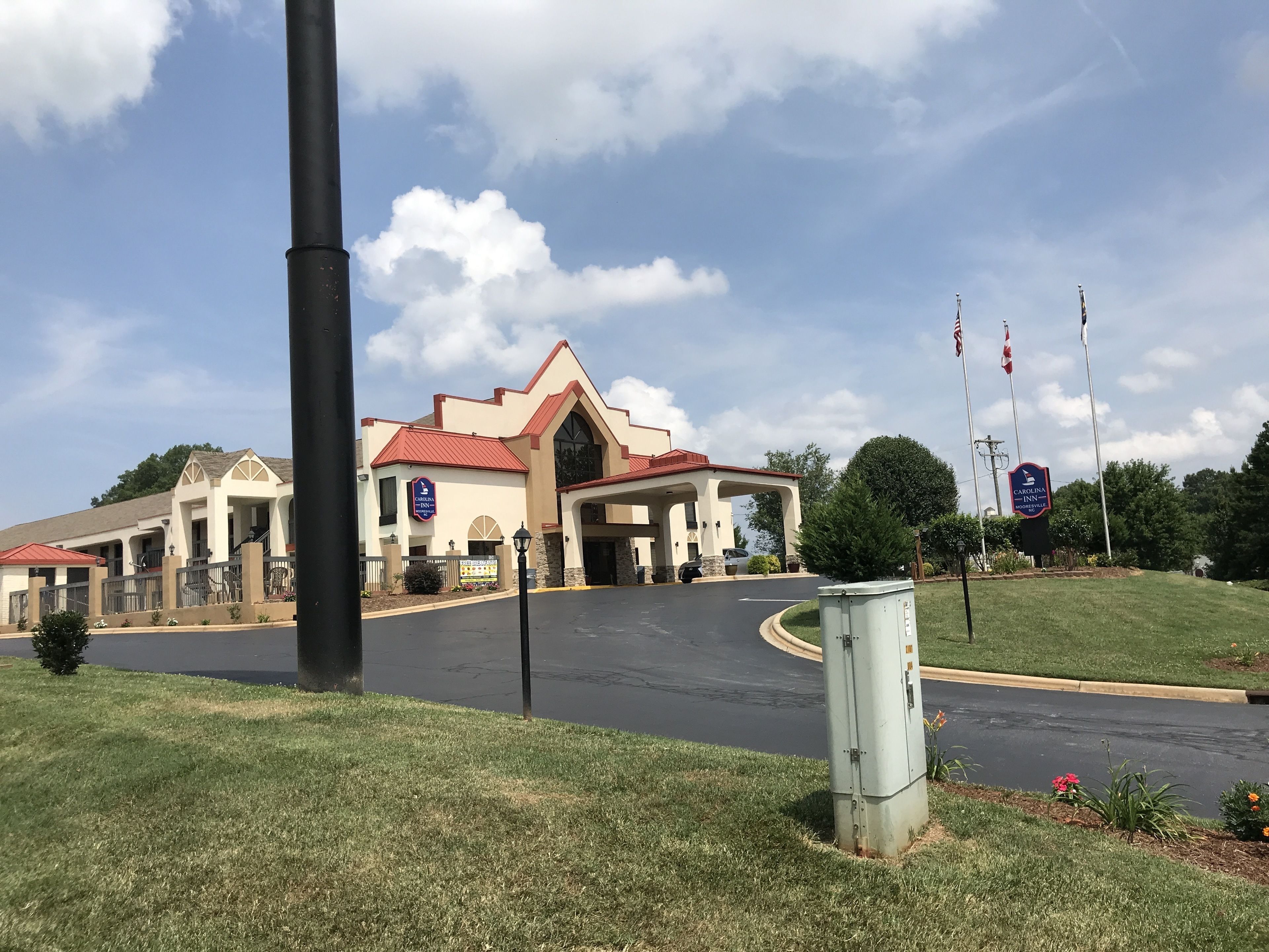 Hotel com telhado vermelho e paredes bege, com entrada espaçosa e área de estacionamento.