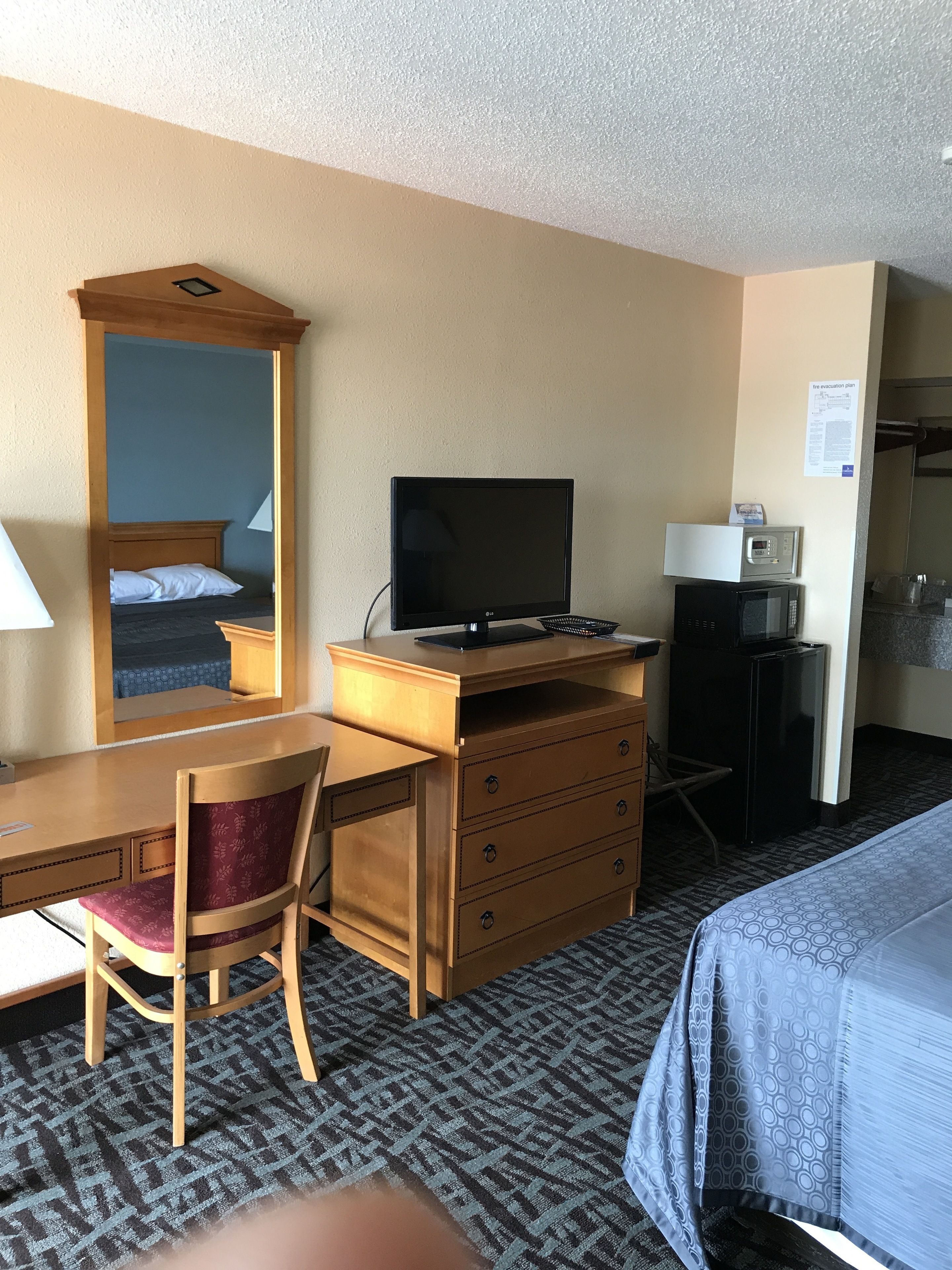 A hotel room with a bed, a desk with a chair, a dresser, a television, a microwave, and a mirror.