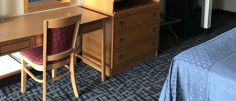 A hotel room with a bed, a desk with a chair, a dresser, a television, a microwave, and a mirror.