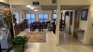 A hotel lobby with a breakfast area, multiple dining tables, chairs, a large rug, and a water fountain. - Carolina Inn & Suites of Lake Norman (Mooresville)