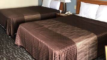 Una habitación de hotel con dos camas, cabecera de madera, lámpara de noche, teléfono y alfombra estampada.