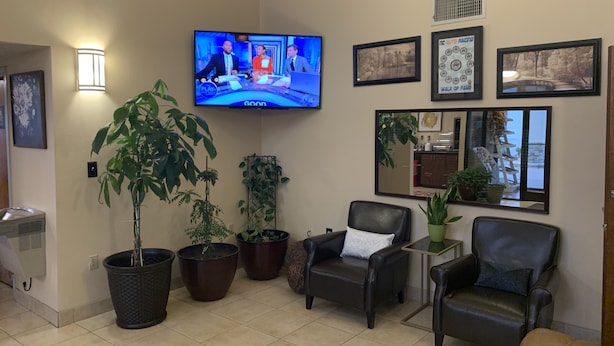 A living room with a flat-screen TV, several potted plants, leather chairs, and framed pictures on the wall. - Carolina Inn & Suites of Lake Norman (Mooresville)