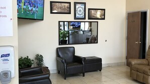 A living room with a flat-screen TV, a chandelier, a black leather armchair, a brown leather sofa, and a small potted plant. - Carolina Inn & Suites of Lake Norman (Mooresville)