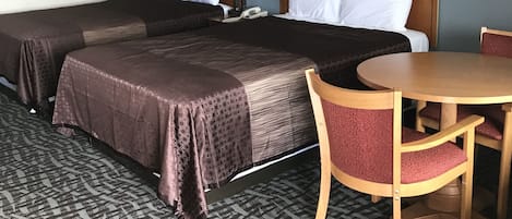 A hotel room with two beds, a dining table, and a chair.