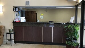 A reception area with a counter, a clock, a sign, and a potted plant. - Carolina Inn & Suites of Lake Norman (Mooresville)