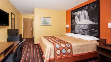 A hotel room with a bed, a desk, a chair, a television, and a framed picture of a waterfall.