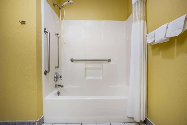 Une salle de bain avec une baignoire blanche, des barres d’appui, une pomme de douche et un porte-serviettes.