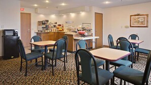 Une chambre d’hôtel dotée d’une kitchenette, d’un coin repas avec tables et chaises, et d’un sol recouvert de moquette.