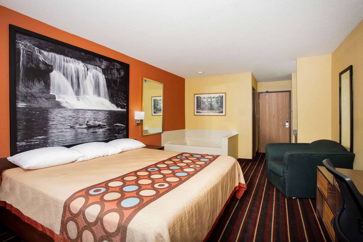 Ein Hotelzimmer mit Bett, Schreibtisch, Stuhl, Bad und einem großen Wandbild.