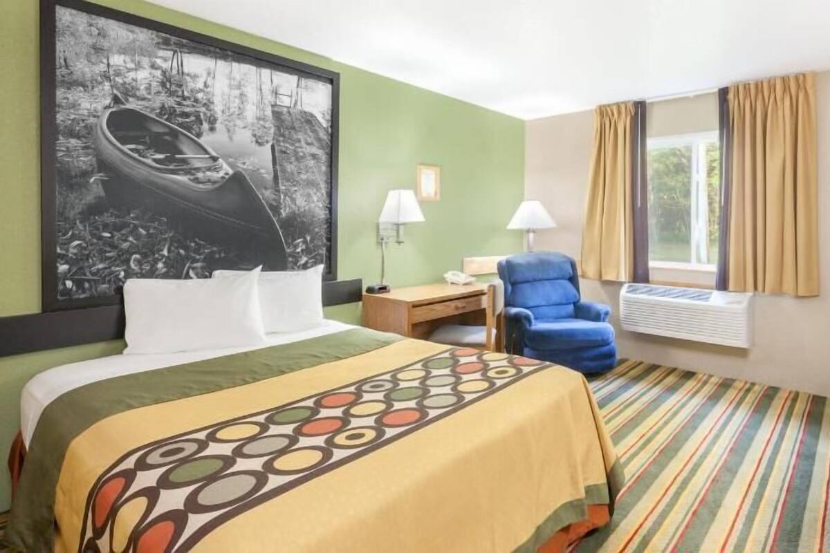 Habitación de hotel con cama, escritorio, silla, televisor y un amplio ventanal con cortinas.