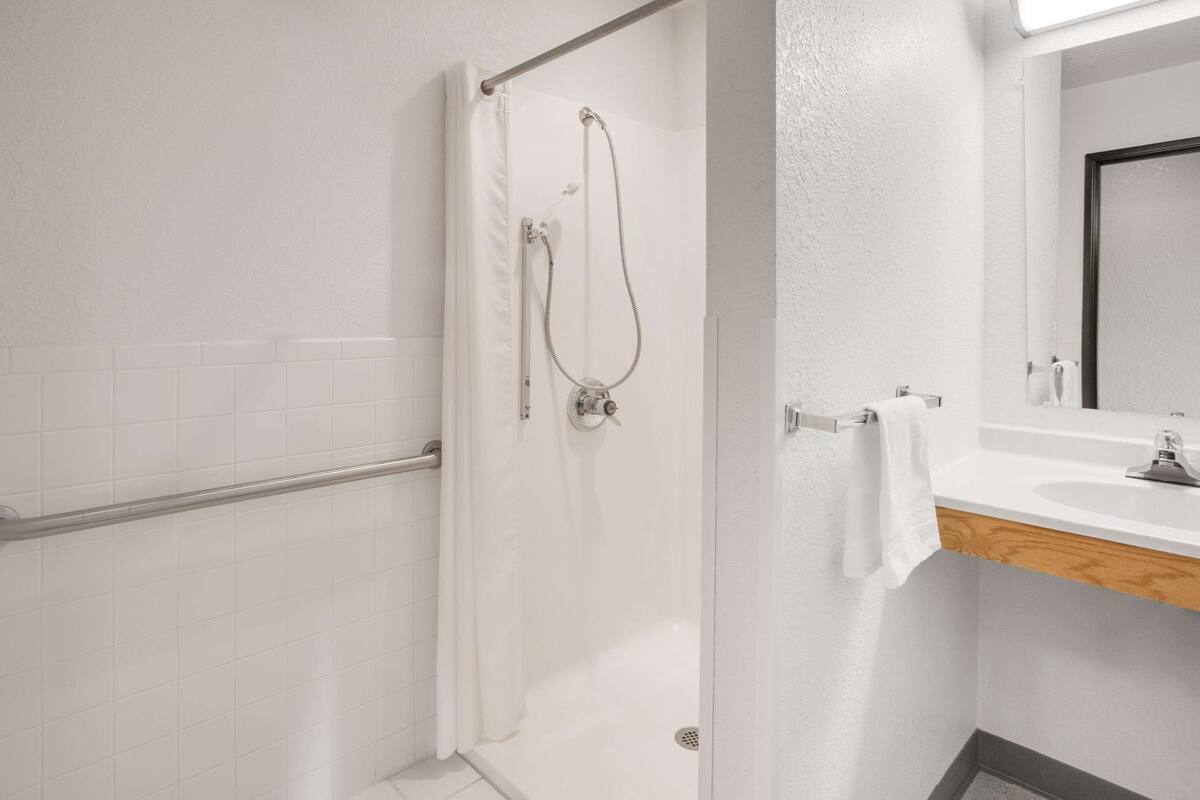 Uma casa de banho moderna com cabine de duche em vidro, lavatório branco e bancada de madeira.