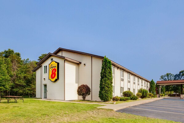 A hotel with a Super 8 sign, a parking lot, and a picnic table. - Super 8 by Wyndham Grayling (Grayling)