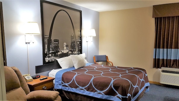 A hotel room with a bed, two bedside lamps, a chair, a desk with a telephone, and a large cityscape poster on the wall.
