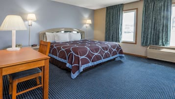 A hotel room with a bed, a desk, two lamps, and a window with curtains.