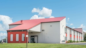 A two-story building with a red roof and white siding, featuring a covered entrance and a small parking area.
