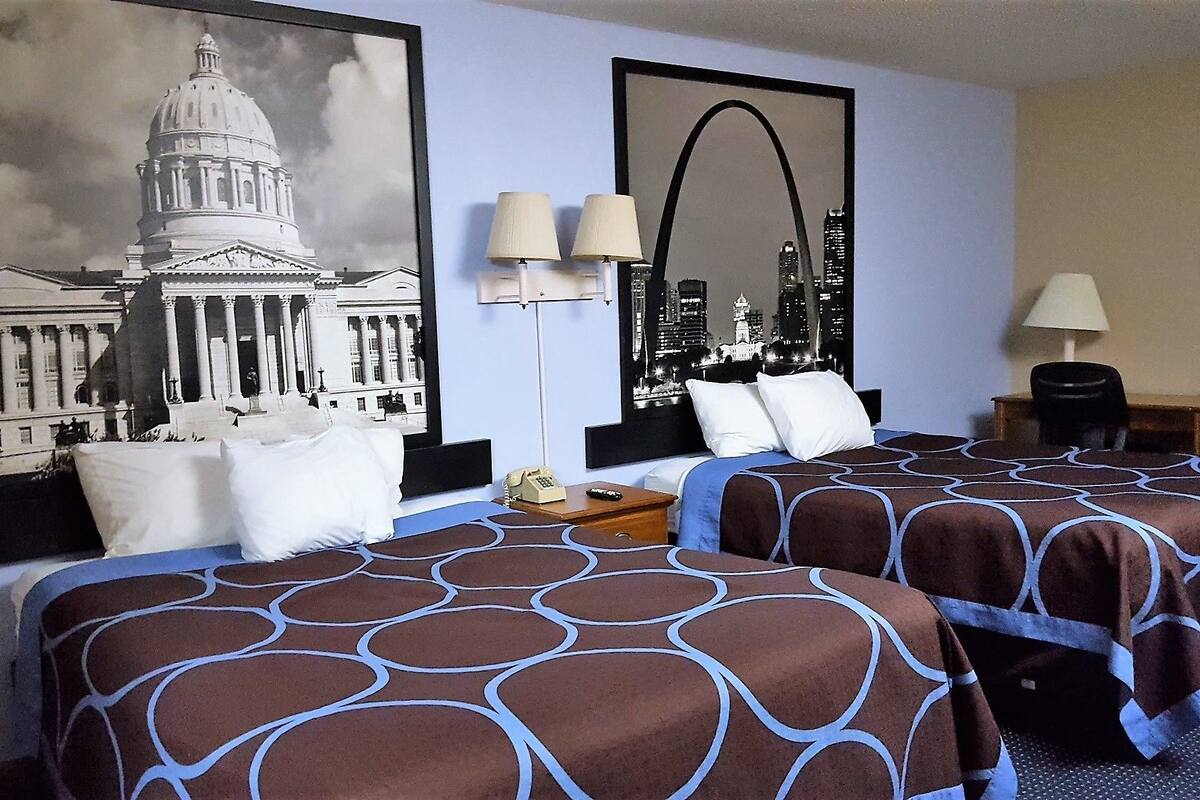 Une chambre d’hôtel avec deux lits, une vue sur la ville et un grand tableau encadré représentant un bâtiment.