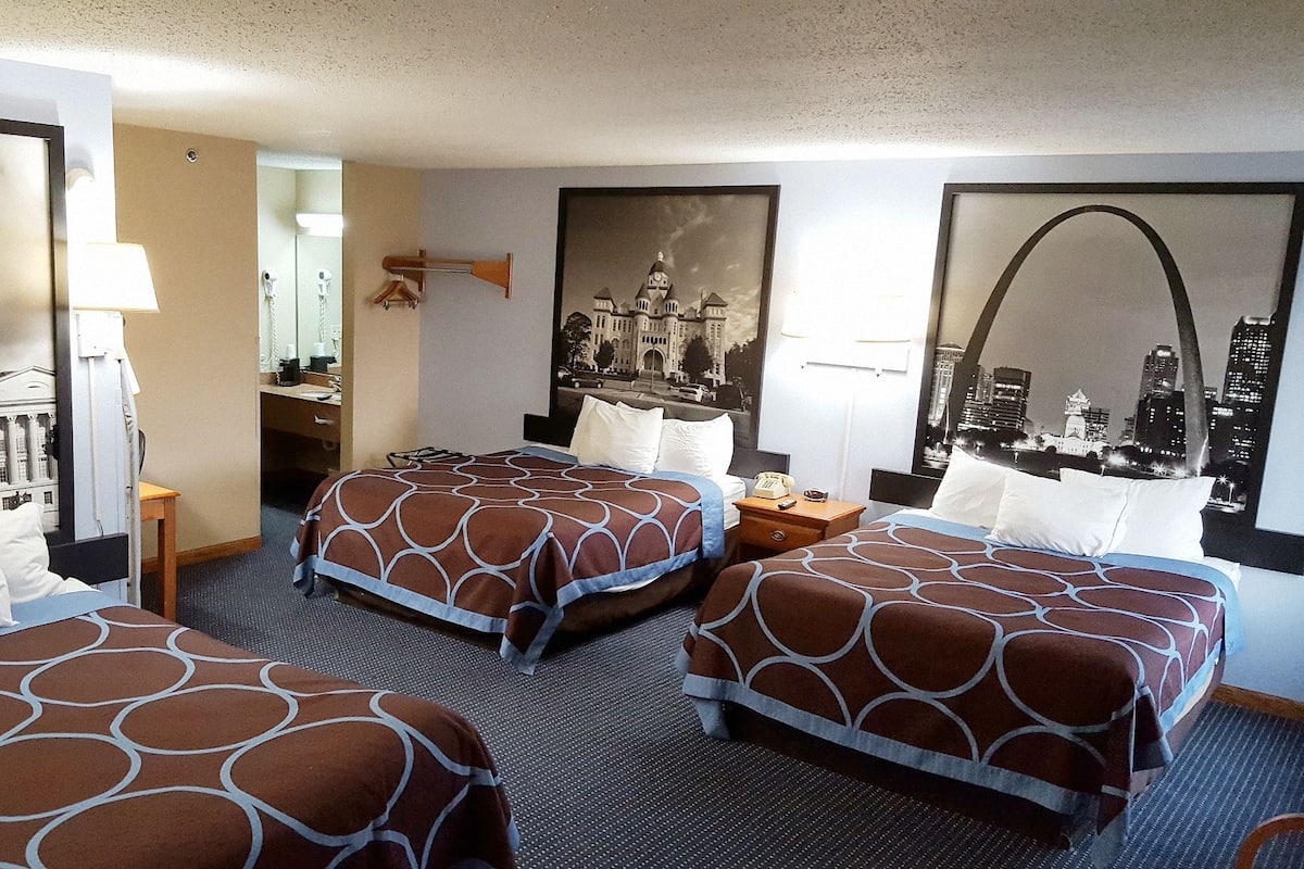 Une chambre d’hôtel avec trois lits, un bureau et un miroir.