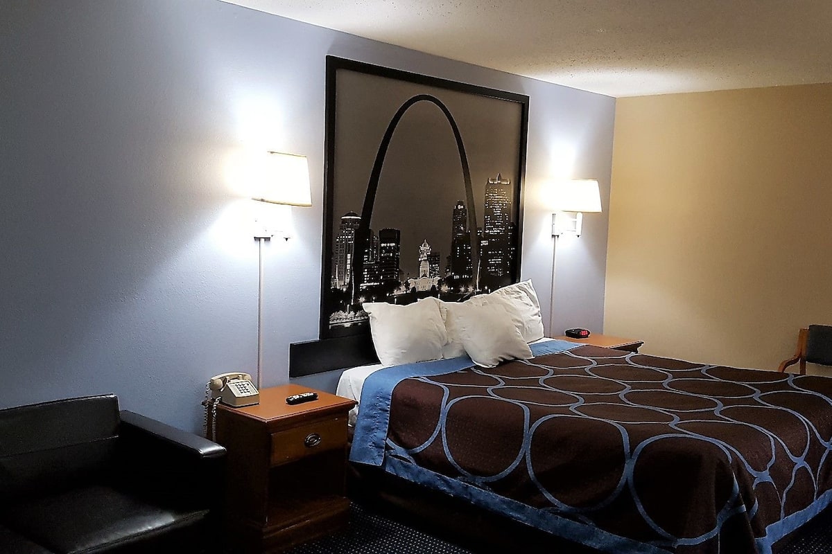 Une chambre d’hôtel comprenant un lit, une table de chevet, une chaise, un bureau et une grande fenêtre donnant sur le paysage urbain.