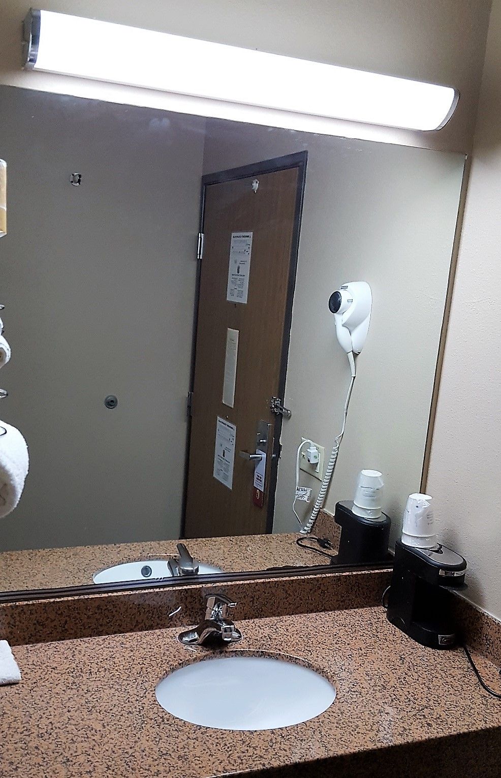 A bathroom with a sink, mirror, and hair dryer mounted on the wall.