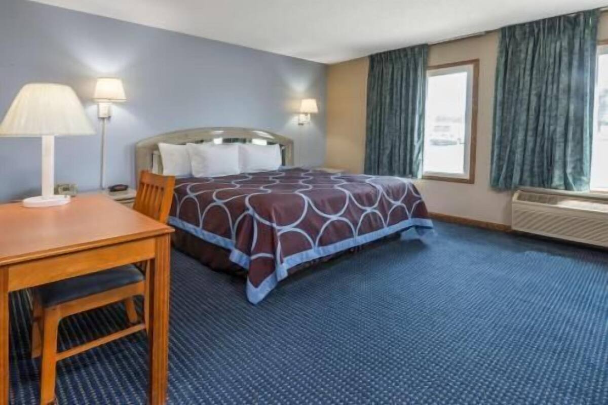 Une chambre d’hôtel avec un lit, un bureau, deux lampes et une fenêtre avec des rideaux.