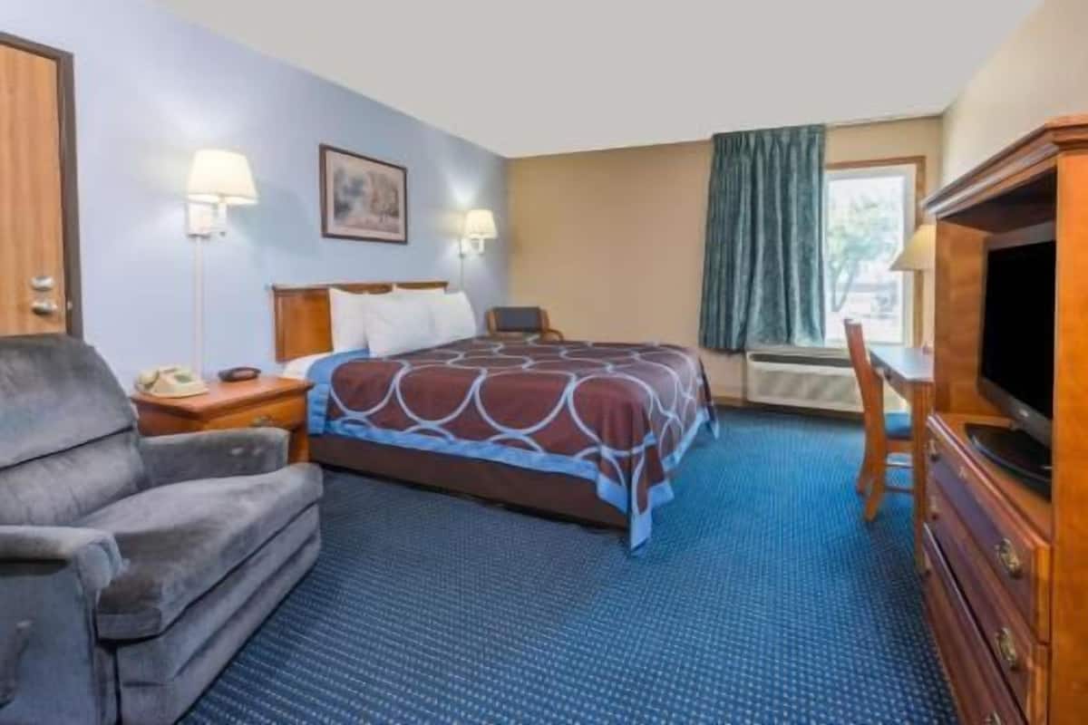 Une chambre d’hôtel équipée d’un lit, d’un bureau, d’une chaise, d’une télévision et d’une fenêtre avec des rideaux.