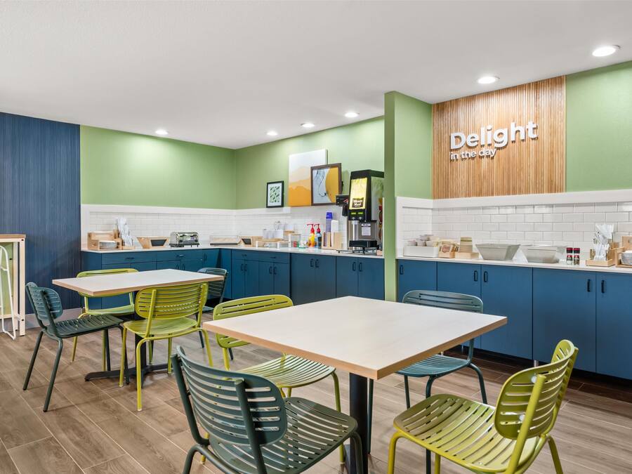 A modern kitchen with teal cabinets, a wooden accent wall, and a 'Delight in the day' sign.