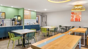 Un café moderne avec des tables en bois et des chaises vertes, un appareil à café et un tableau affichant le menu.