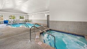 Une piscine intérieure avec un bord carrelé de bleu, un panneau indiquant qu’il est interdit de plonger, et une chaise bleue près de la piscine.