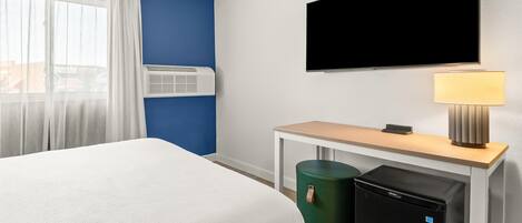Une chambre d’hôtel équipée d’un lit, d’un bureau, d’une télévision, d’une lampe et d’un mini-réfrigérateur.