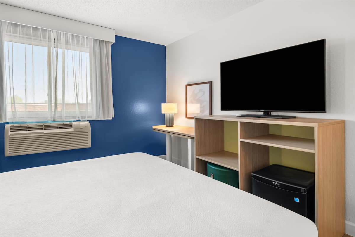 A hotel room with a bed, a desk with a lamp, a television, a heater, and a wardrobe.