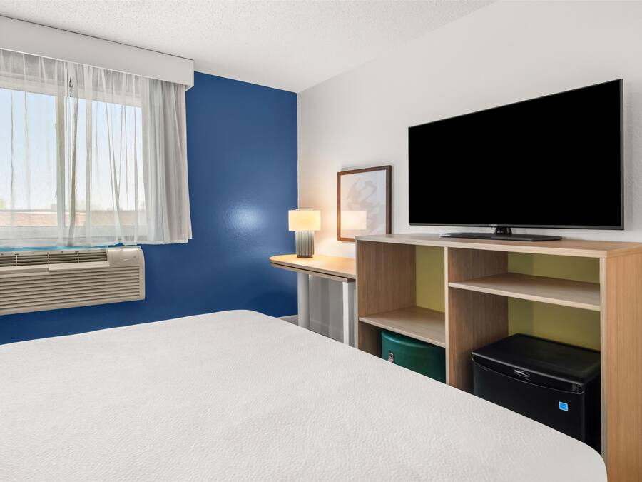 A hotel room with a bed, a desk with a lamp, a television, a heater, and a wardrobe.