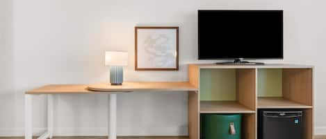A modern room with a wooden desk, a flat-screen TV, a lamp, and a small cabinet with a trash bin.