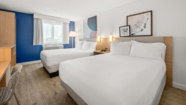 Une chambre d’hôtel avec deux lits, un bureau, une chaise et une fenêtre avec des rideaux.