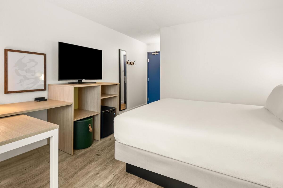 A modern hotel room with a bed, a flat-screen TV, a desk, and a wardrobe.