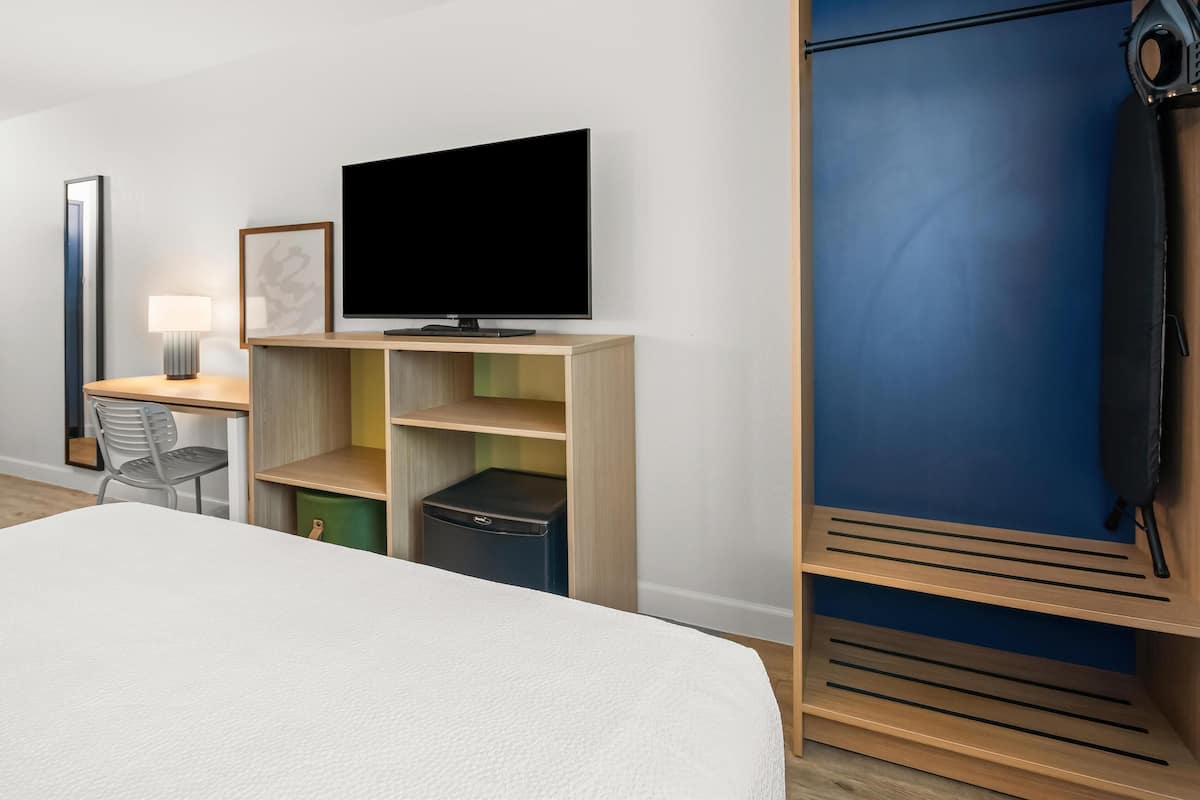 A hotel room with a bed, a desk with a lamp, a television, and a wardrobe.