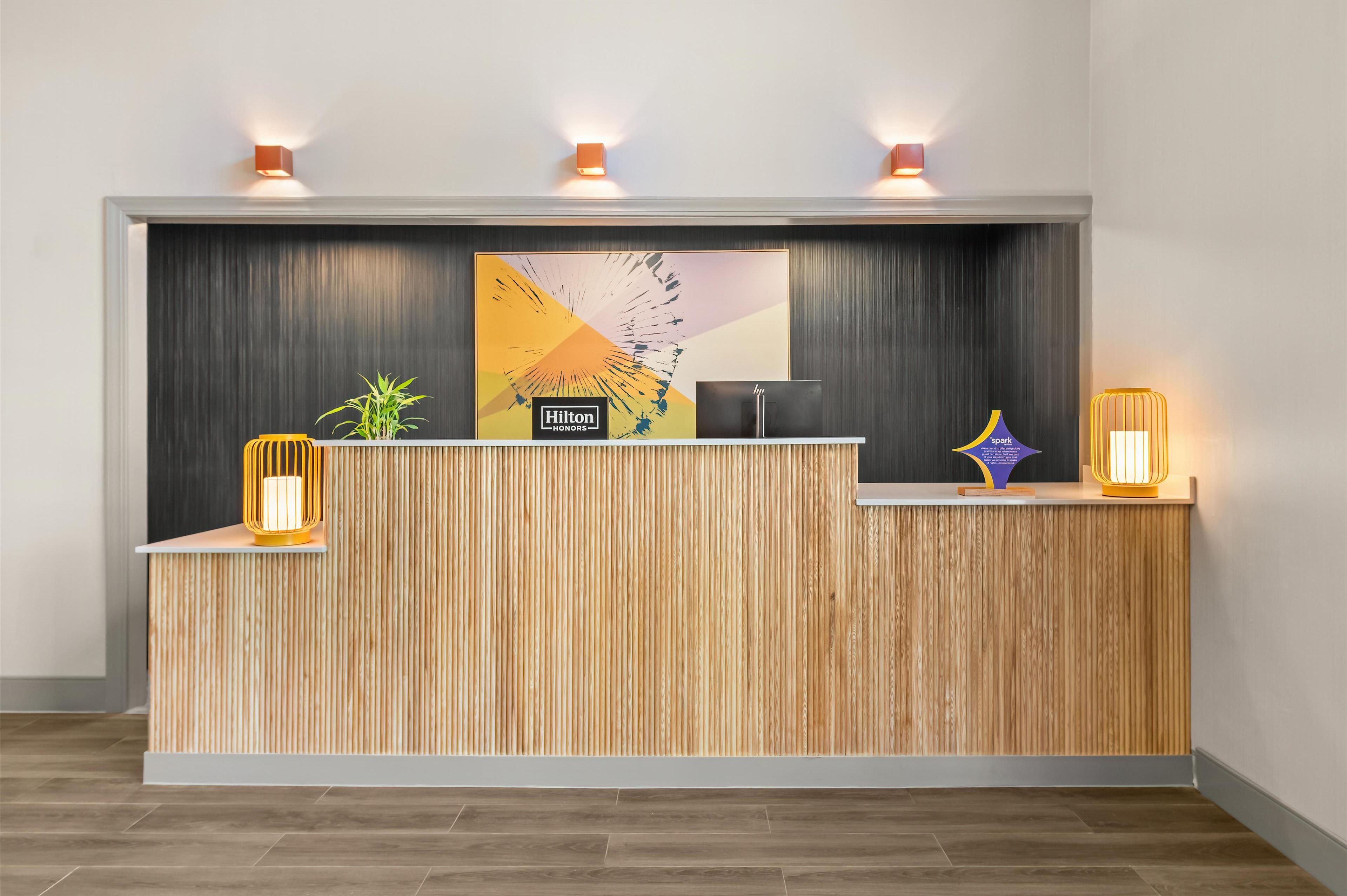 Un mostrador de recepción de hotel con detalles de madera, un gran logotipo de Hilton Honors y dos lámparas fijadas a la pared.
