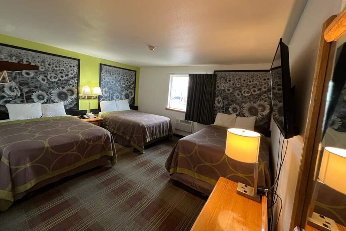 A hotel room with two beds, a desk, a TV, and a window with curtains.