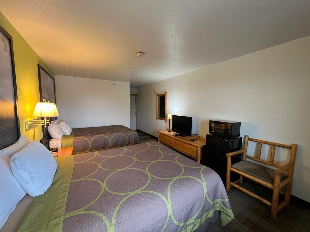 A hotel room with two beds, a desk with a television, a chair, and a lamp.