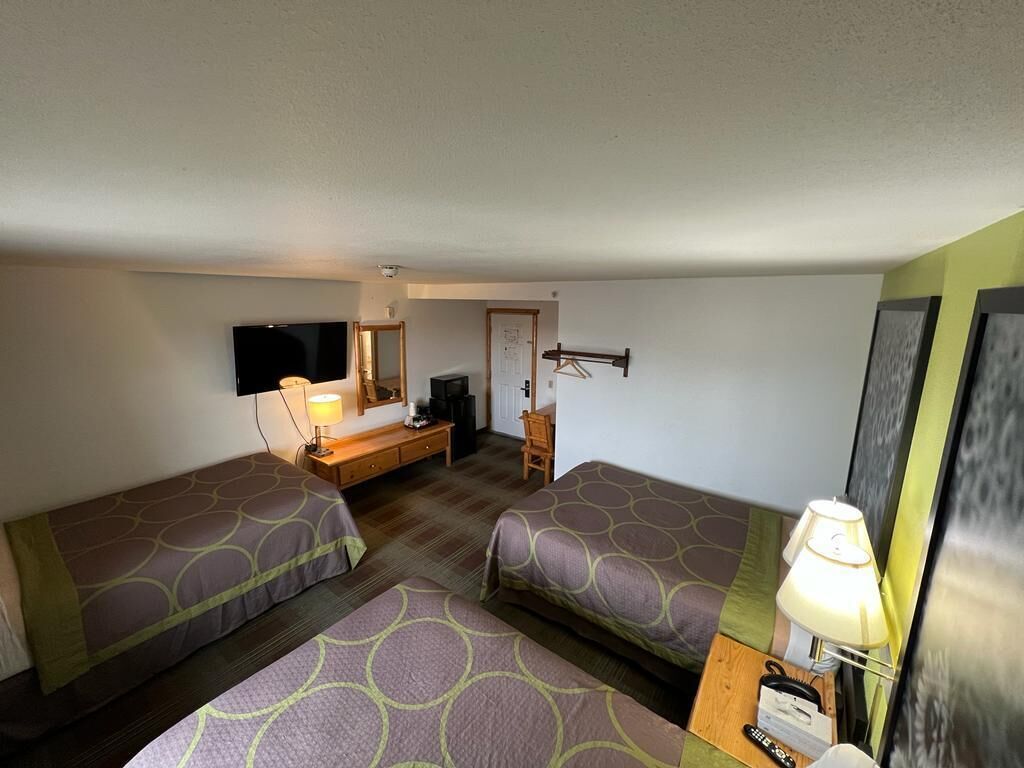 A hotel room with two single beds, a desk with a chair, a television, and a lamp.