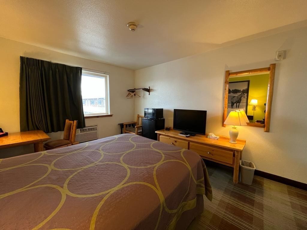 Et hotelværelse med en stor seng, et skrivebord med en computer, et fjernsyn og en lampe.